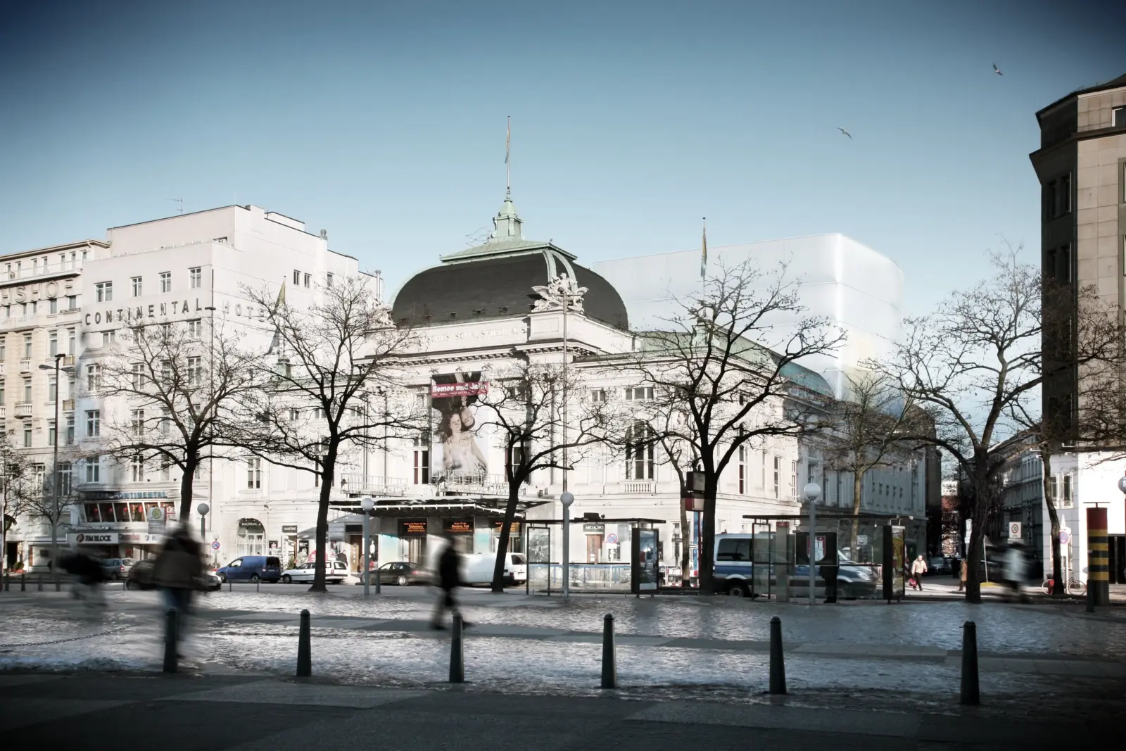 Ein heller, kubischer Baukörper ergänzt hinter einem historischen Kuppelbau die Platzansicht mit kahlen Bäumen im Vordergrund.