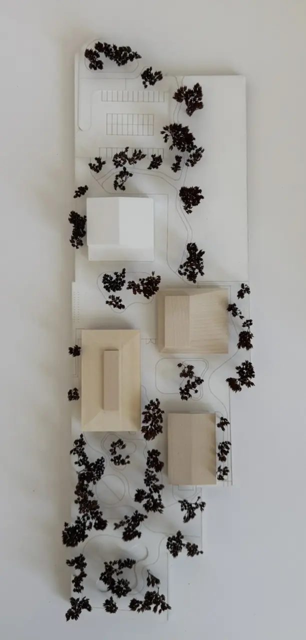 Modellfoto von oben zeigt mehrere quaderförmige Baukörper, umgeben von dunklen Bäumchen aus Modellbaumaterial.