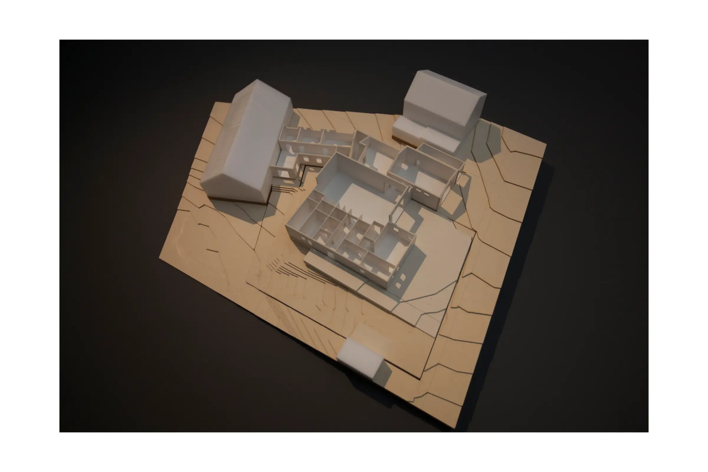 Modellfoto eines Gebäudekomplexes mit Erdgeschossgrundriss auf einer Geländeplatte aus Holz, umgeben von zwei Nachbarbauten.