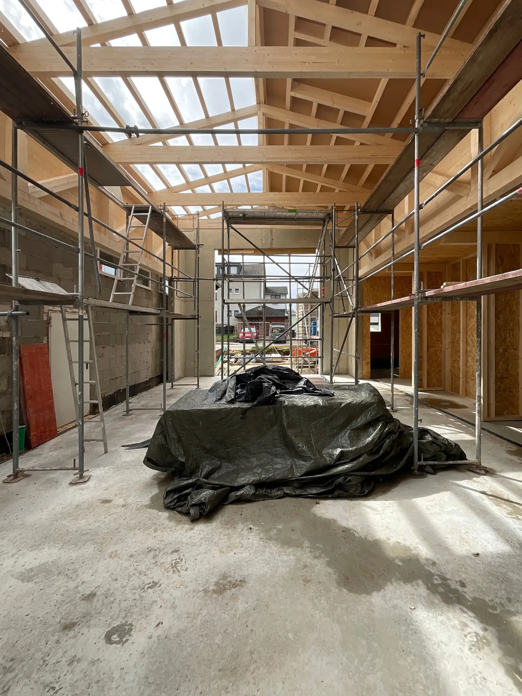 Baustellenfoto einer Halle im Rohbau mit sichtbarem Holzdachtragwerk und Gerüsten an beiden Längsseiten.