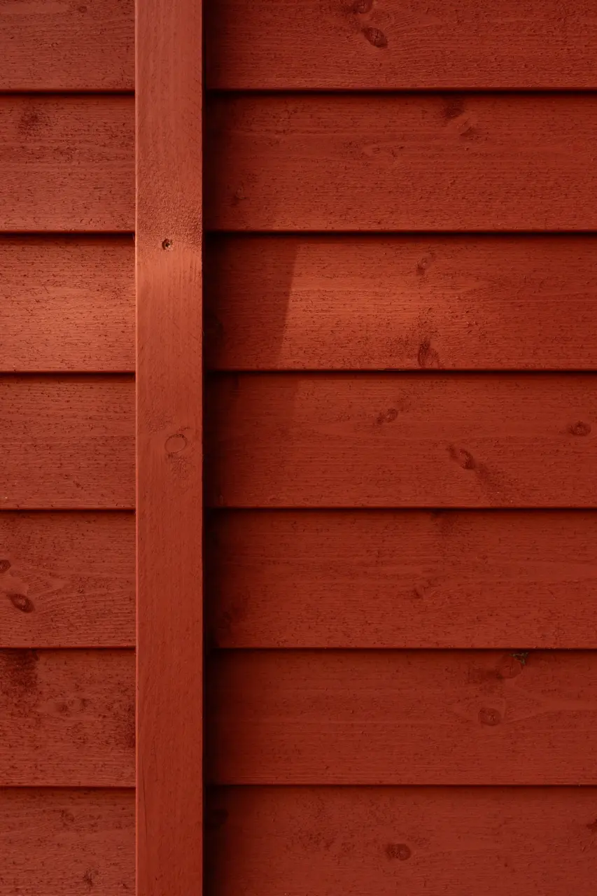 Nahaufnahme einer rotbraun lasierten Holzfassade mit horizontal verlegten Brettern und einer vertikalen Latte.