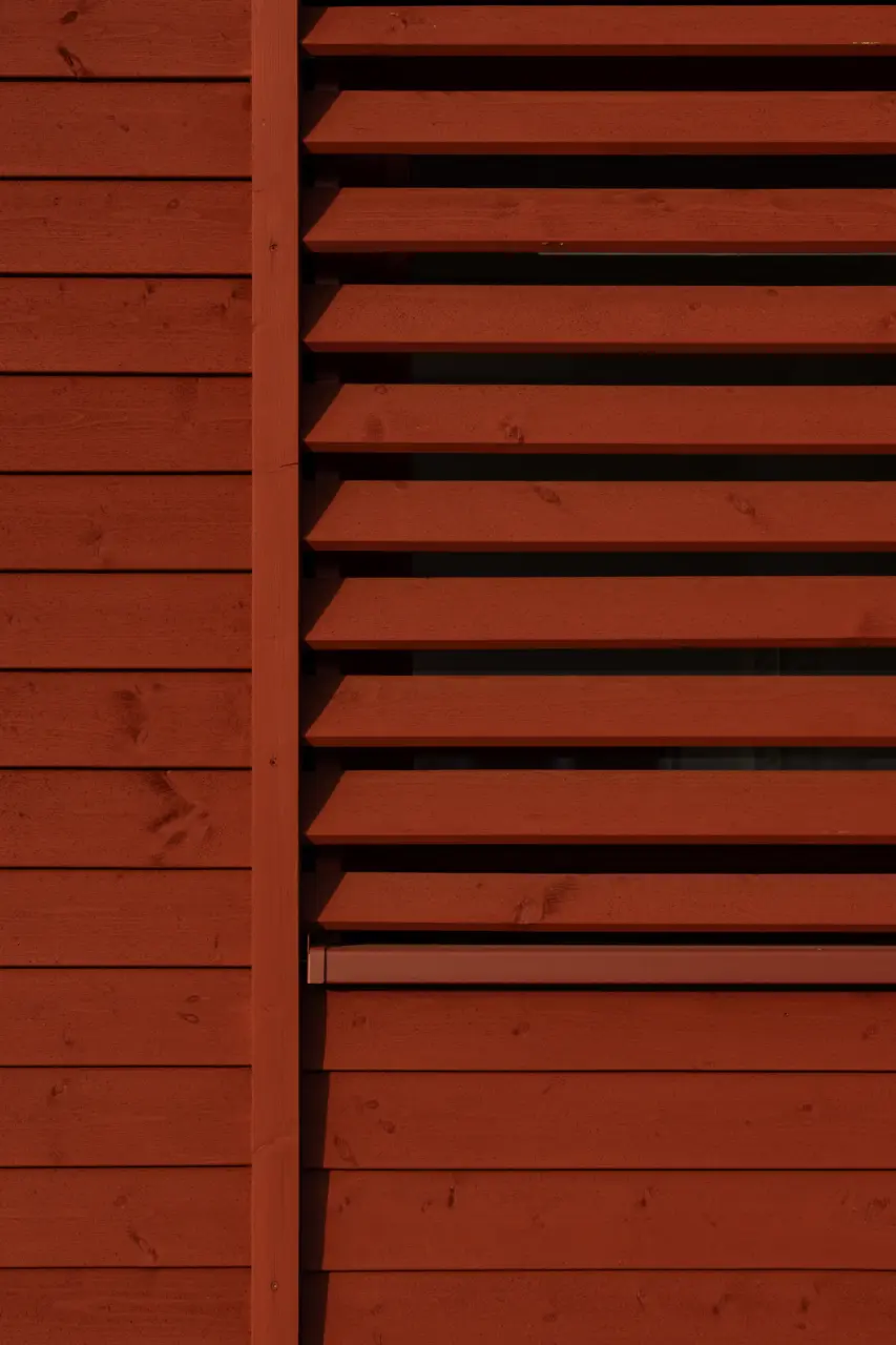 Fassadendetail mit horizontaler Holzschalung und vorgesetzten Holzlamellen als Sonnenschutz vor der Fensterfläche.