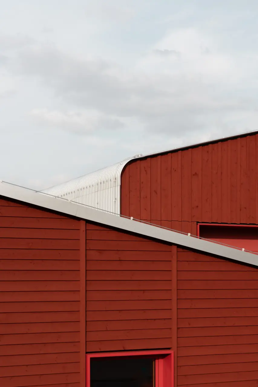 Detailansicht der roten Holzfassade zeigt eine geschwungene Dachkante mit weißer Wellblechverkleidung.