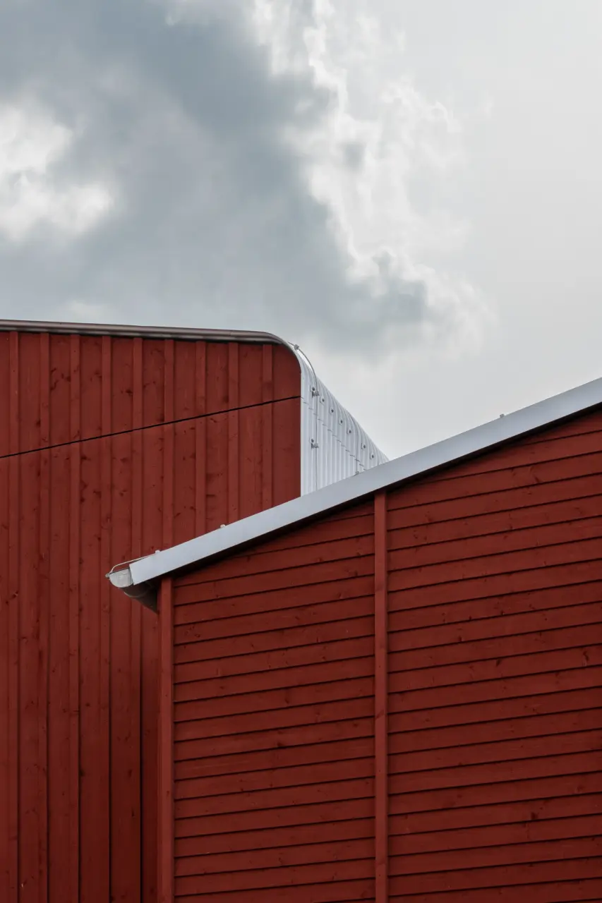 Giebel eines Holzbaus mit horizontaler Lattung, Zinkblech-Dachrand und Regenrinne vor bewölktem Himmel.