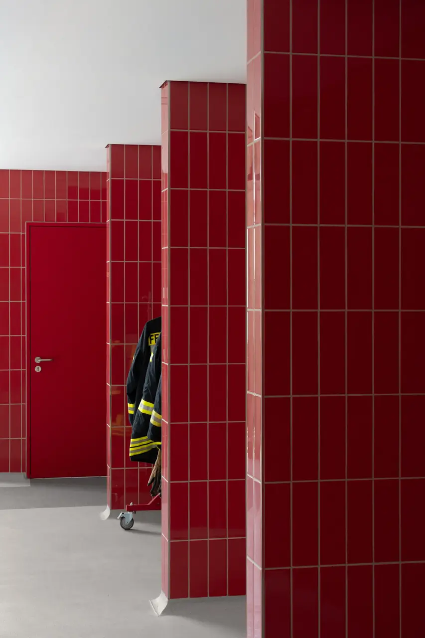 Innenraum einer Feuerwache mit rot gefliesten Wandpfeilern, an einem hängt eine Einsatzjacke.