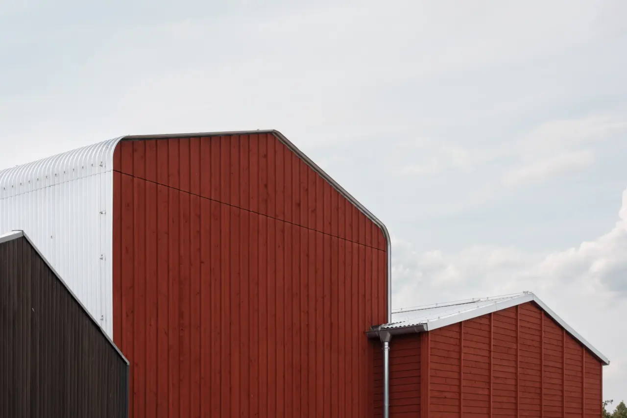 Giebelfassade mit vertikaler Holzverschalung in Rot und Dunkelbraun, Dachrand aus profiliertem Metallblech.
