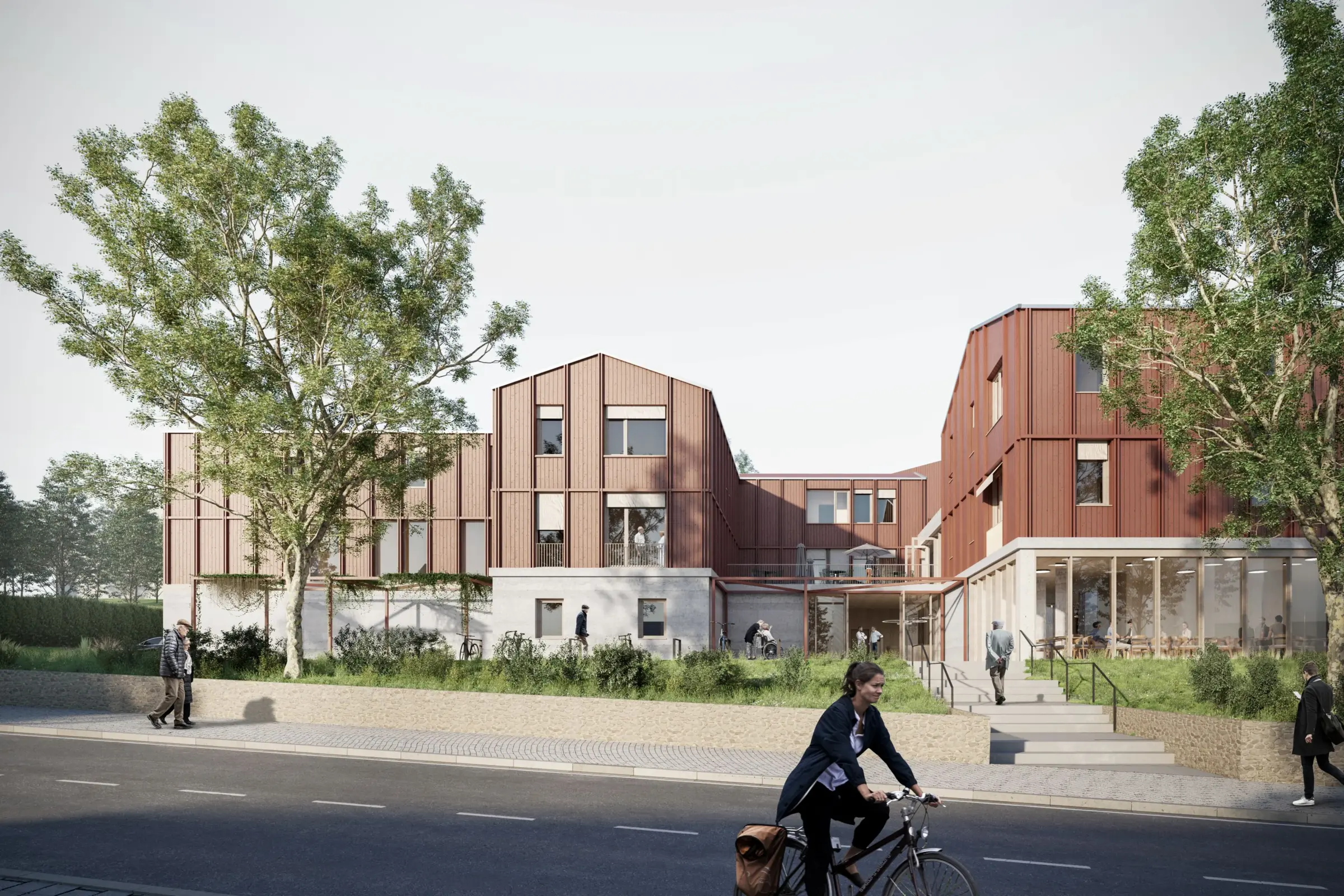 Aussenperspektive eines mehrteiligen Gebäudekomplexes mit Satteldächern und rötlicher Metallfassade, davor Eingangsbereich mit Freitreppe.